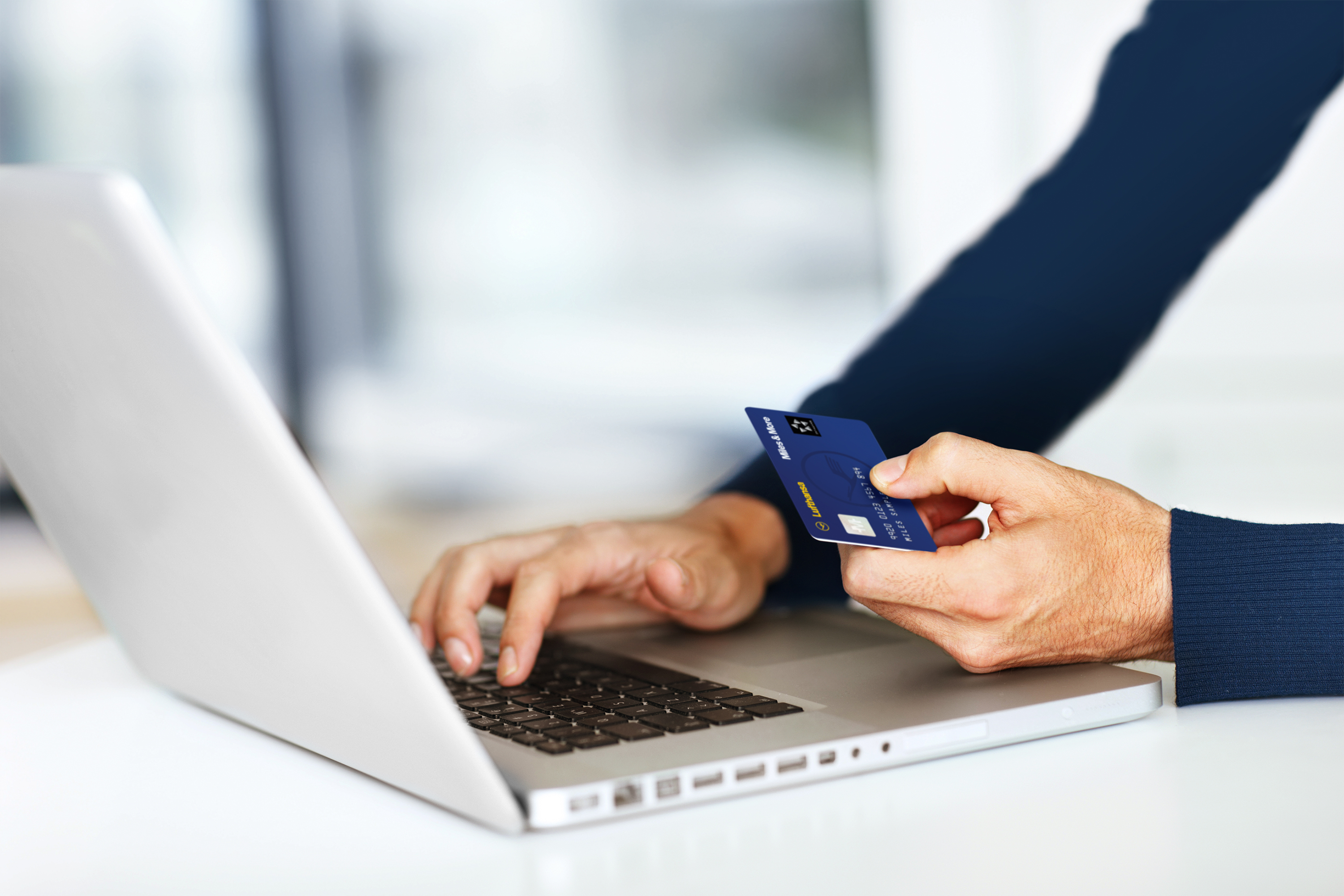 Person with laptop and Lufthansa Miles&More credit card