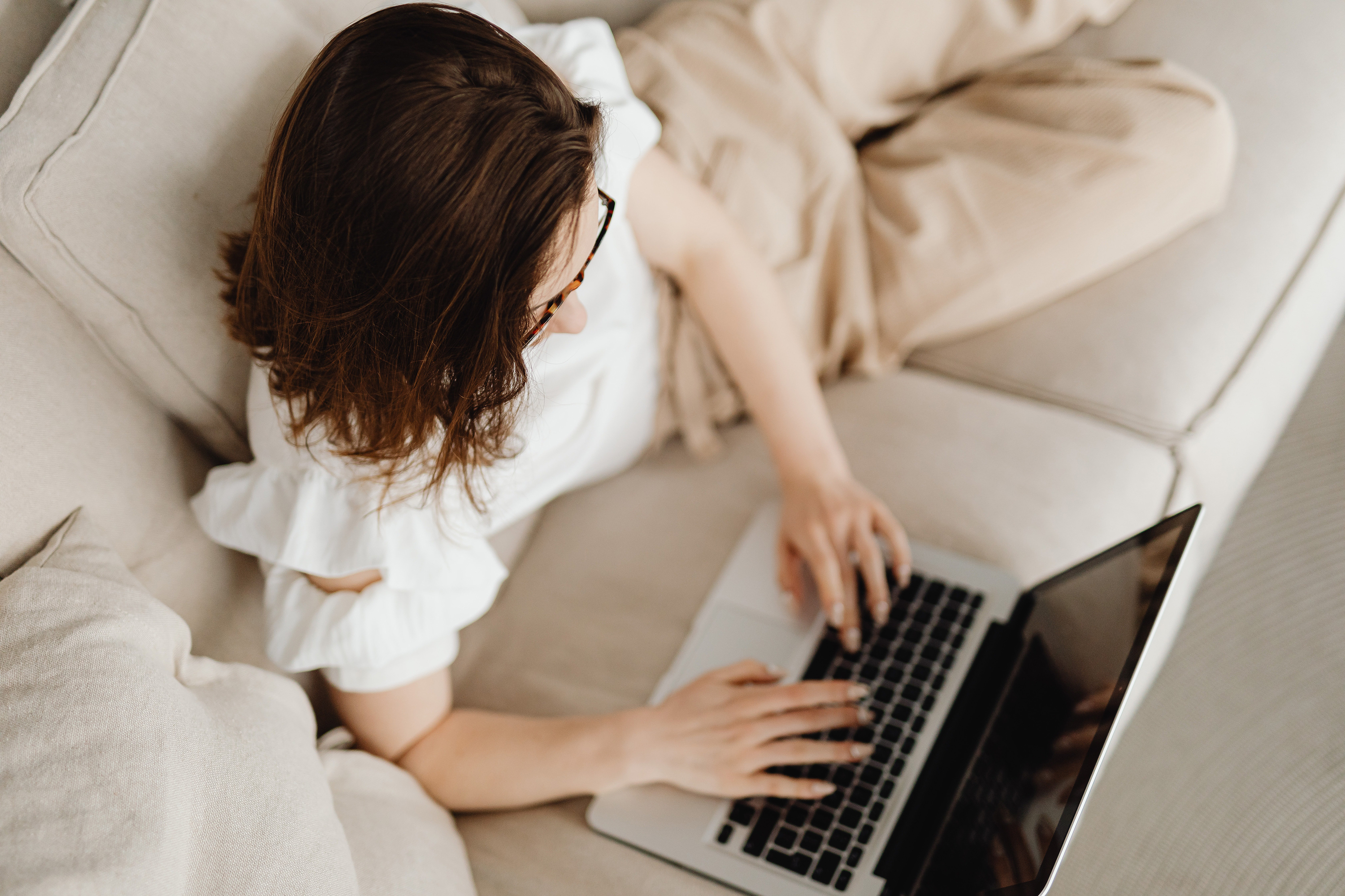 A woman lies on the sofa with her laptop and uses online check-in